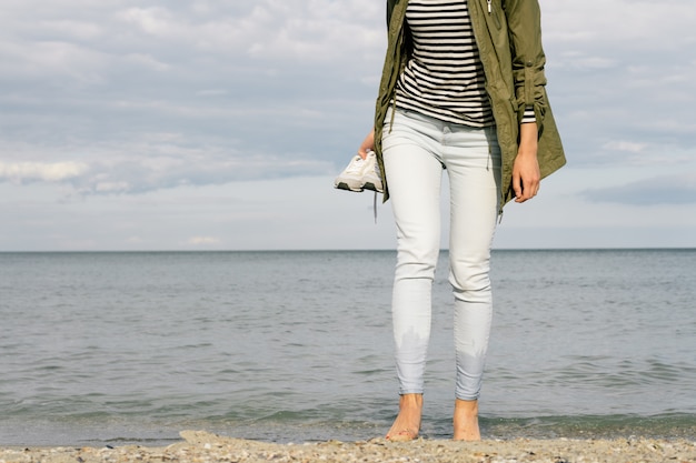 Mujer caminando descalza en la playa y sosteniendo un zapato en la mano