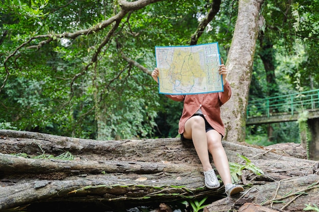 Mujer caminando y mirando el mapa al aire libre en la naturaleza Viajeros exploran el mapa del bosque montañoso Mujer con camisa a cuadros roja sosteniendo un mapa en el bosque