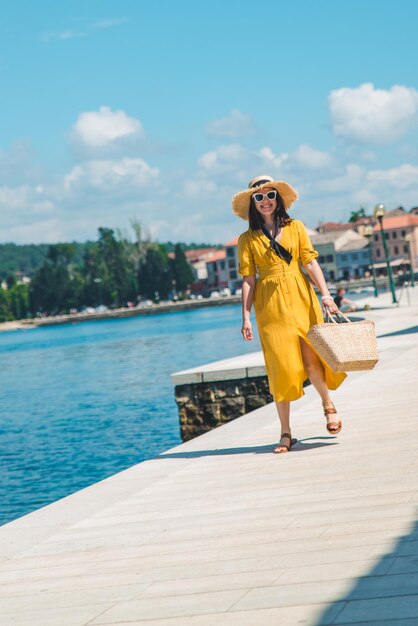 Mujer caminando por el muelle del mar en un día de verano con vestido amarillo