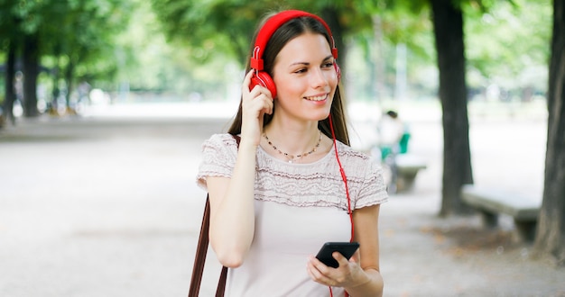 Mujer caminando en un parque mientras usa su teléfono inteligente para escuchar música