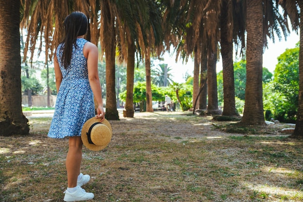 Mujer caminando por el parque de palmeras con vestido azul. vacaciones de verano