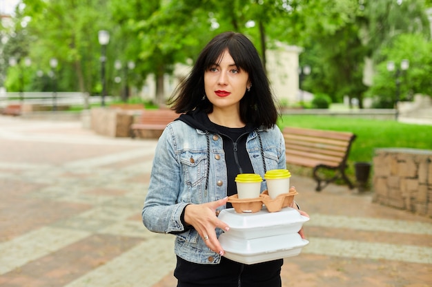 Mujer caminando en el parque, sosteniendo una comida para llevar y café, almorzando del trabajo.