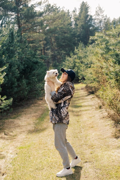 Mujer caminando con un perro maltés blanco en un sendero forestal