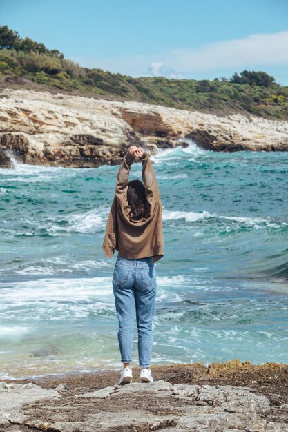 Mujer caminando por la playa de mar rocoso en las vacaciones de verano de un día soleado y ventoso