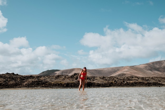 Foto mujer caminando en la playa y rocas volcánicas