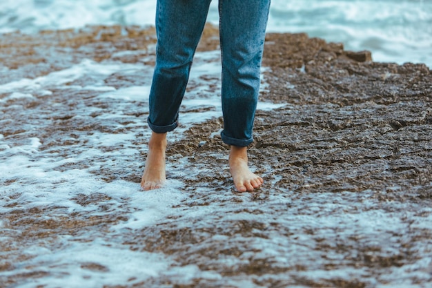 Mujer caminando por la playa rocosa descalzo jeans mojados