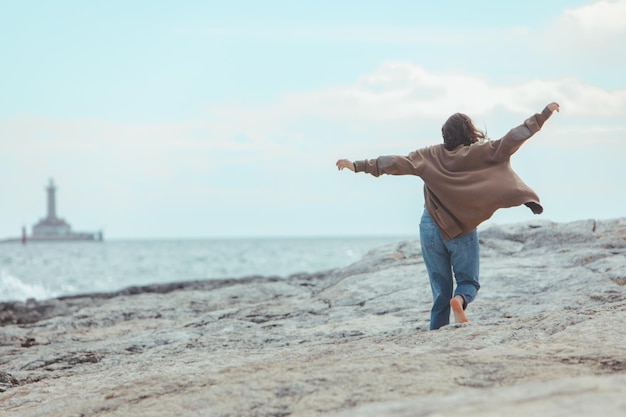 Mujer caminando por la playa rocosa en el faro de jeans mojados en el fondo