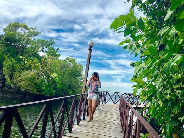 Mujer caminando por un puente peatonal contra el cielo