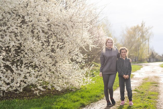 Mujer caminando con su hija en un floreciente jardín de primavera explorando un árbol en flor. La familia admira la naturaleza.