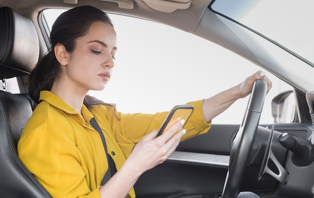 Foto mujer en camisa amarilla conduce y usa su teléfono