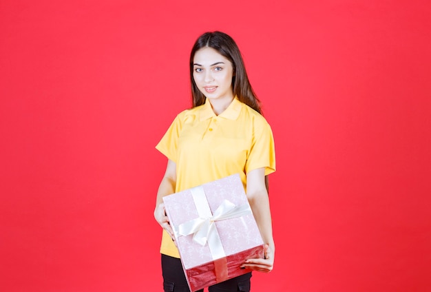 mujer con camisa amarilla sosteniendo una caja de regalo rosa.