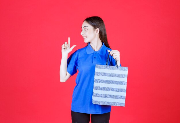 mujer con camisa azul sosteniendo una bolsa de compras a rayas azules.