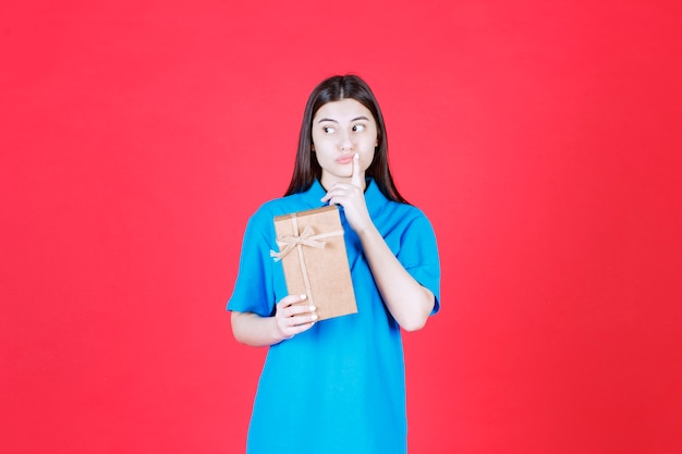 mujer con camisa azul sosteniendo una caja de regalo de cartón mini y parece confundida.