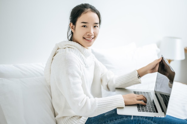 Una mujer con una camisa blanca en la cama y jugando a la computadora portátil felizmente