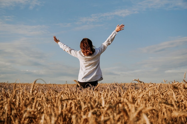 Una mujer con una camisa blanca en un campo de centeno. Vista desde atrás. El concepto de pacificación, meditación, felicidad, armonía.