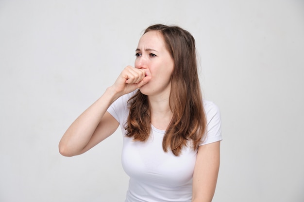 Una mujer con una camisa blanca estornuda y tose de resfriados y gripe.