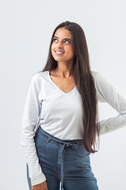 Una mujer con una camisa blanca de manga larga y jeans se para frente a un fondo blanco.