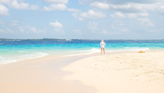 Mujer con camisa blanca de pie en la orilla y mira al océano
