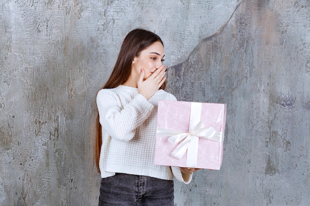mujer con camisa blanca sosteniendo una caja de regalo púrpura y haciendo chismes.