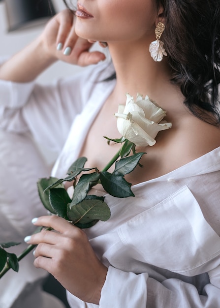 Mujer con camisa blanca sostiene una rosa en sus manos.