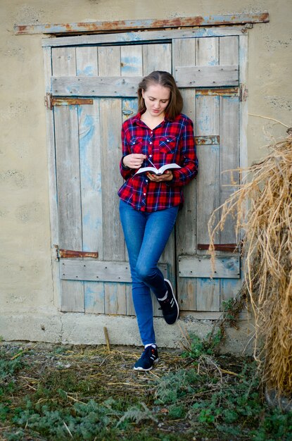 Mujer en una camisa a cuadros y jeans leyendo un libro, de espaldas a la puerta