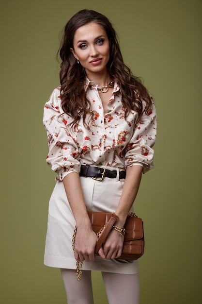 Mujer en camisa estampada falda blanca medias zapatos marrones accesorios de bolso sobre fondo verde