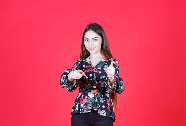 mujer con camisa floral de pie sobre la pared roja y notando a la persona que está delante.