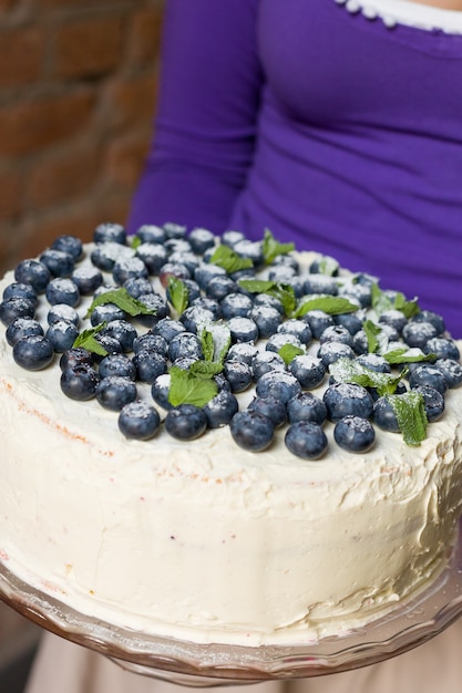 Mujer en camisa lila con tarta de cumpleaños blanca casera festiva con arándanos orgánicos y menta