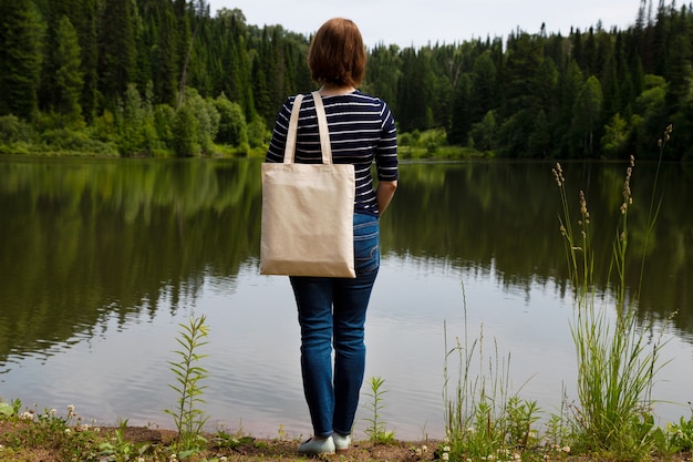 Mujer en la camisa de manga larga a rayas con maqueta de bolsa de compras con vista al río de verano