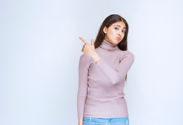 Foto mujer con camisa morada mostrando algo a la izquierda.