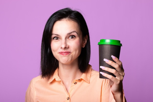 mujer con camisa naranja sostiene una taza de café en sus manos fondo rosa