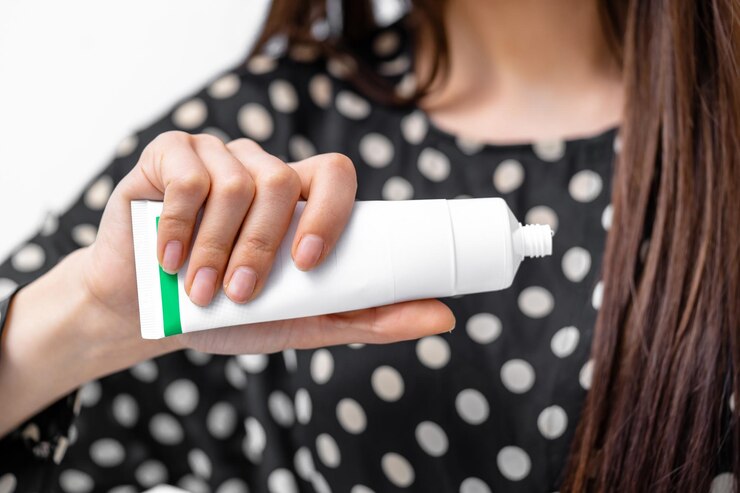 Foto mujer con camisa de puntos polka sostiene un tubo de crema en el interior una persona sosteniendo un tubo de crema con una etiqueta verde en un entorno interior brillante