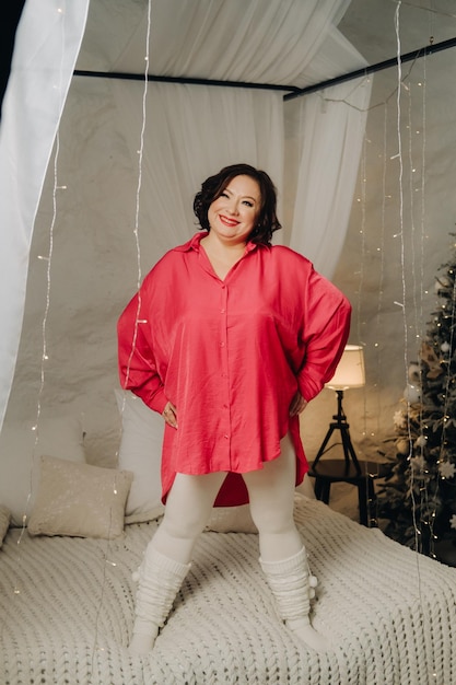 Una mujer con una camisa roja está parada en el dormitorio en una cama decorada para el ambiente de Año Nuevo de Navidad en casa