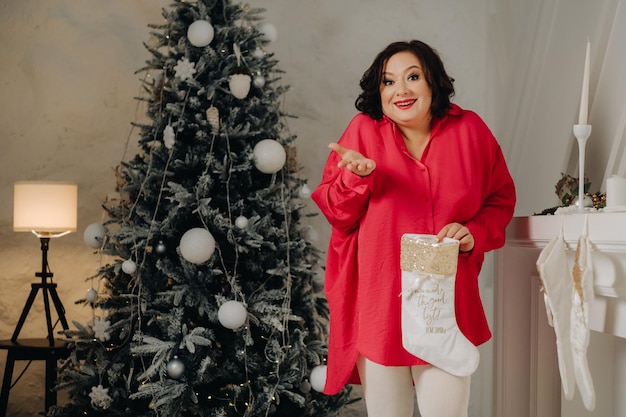Una mujer con una camisa roja en la habitación mira un regalo en un calcetín de Santa Claus decorado para la atmósfera de Navidad en casa de Año Nuevo