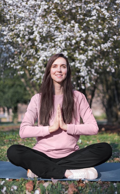 Foto una mujer con una camisa rosa se sienta en una pose de yoga con un árbol al fondo.