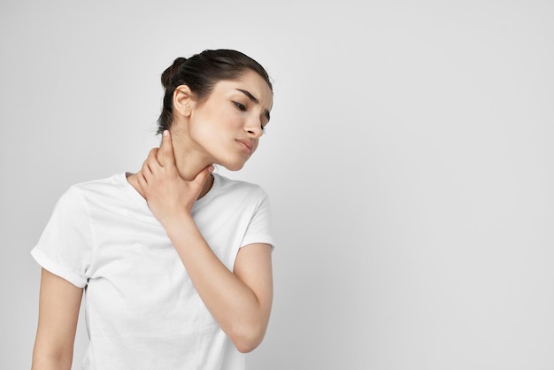 Mujer en una camiseta blanca dolor en el cuello fondo claro