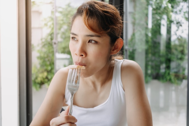 Mujer en camiseta blanca está desayunando con un tenedor