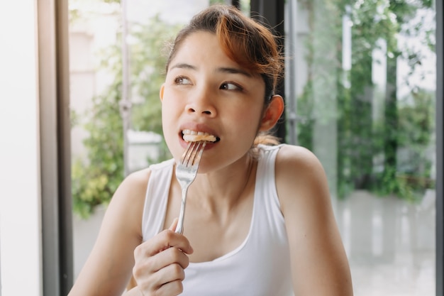 Mujer en camiseta blanca está desayunando con un tenedor