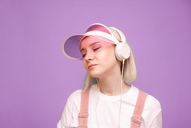 Mujer con camiseta blanca y gorra rosa, escucha música en sus auriculares