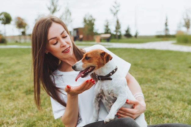 Una mujer con una camiseta blanca y jeans abraza a su perro Jack Russell Terrier en la naturaleza en el parque Mejores amigas leales desde la infancia Estilo de vida