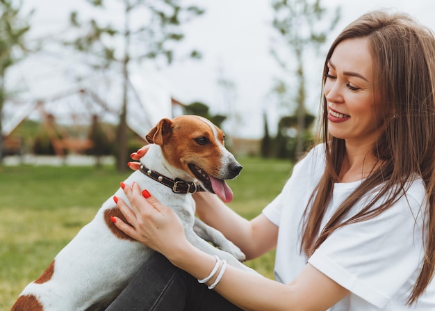 Una mujer con una camiseta blanca y jeans abraza a su perro Jack Russell Terrier en la naturaleza en el parque Mejores amigas leales desde la infancia Estilo de vida