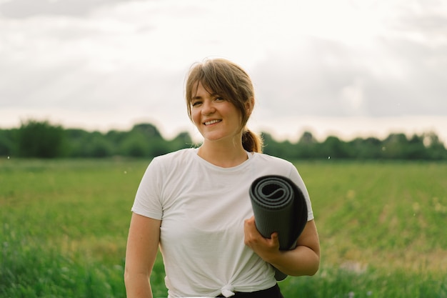 Mujer en una camiseta blanca y leggings haciendo yoga en un hermoso campo en un estilo de vida de estera deportiva