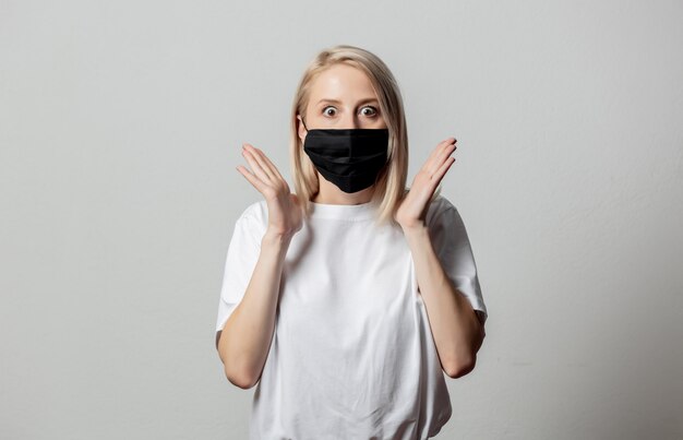 Mujer con camiseta blanca y mascarilla negra sobre pared blanca