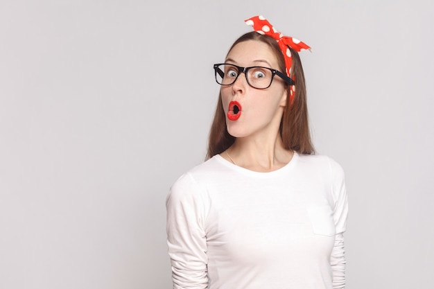 Mujer en camiseta blanca con pecas, gafas negras, labios rojos y banda para la cabeza