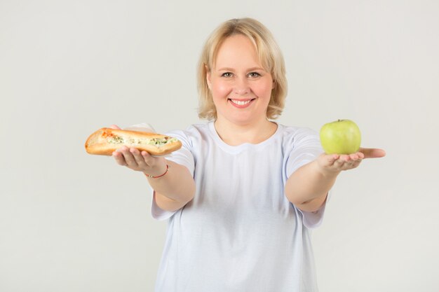 Mujer con una camiseta blanca con un sándwich y una manzana