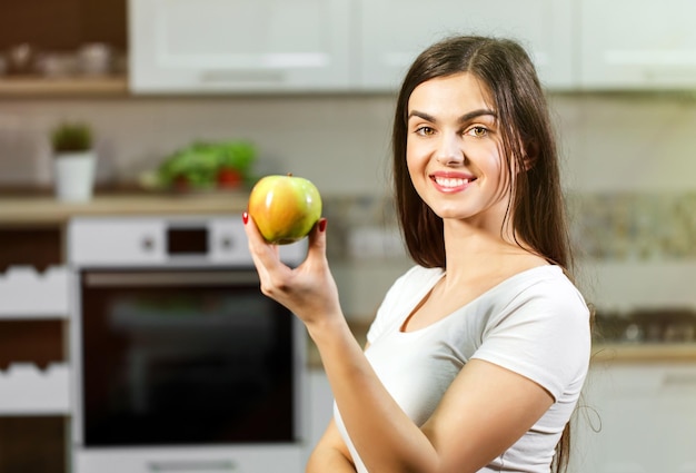 Mujer con camiseta blanca sosteniendo manzana verde en la cocina