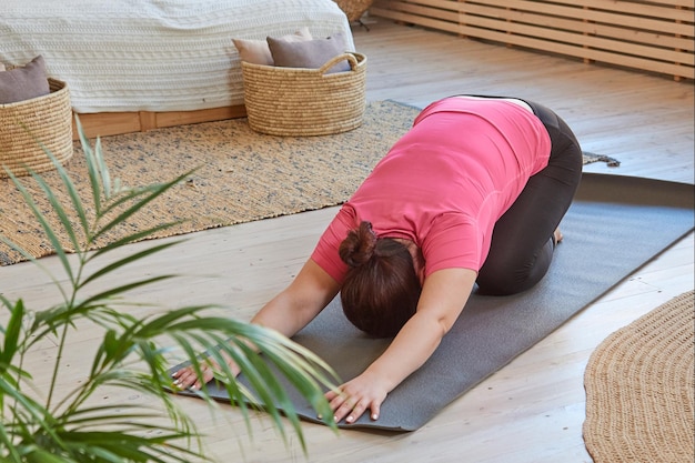 Mujer en camiseta carmesí haciendo ejercicio de estiramiento haciendo deportes en casa en el tatami