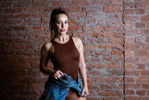 Foto una mujer con una camiseta marrón está de pie frente a una pared de ladrillo