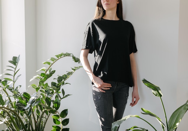 Mujer con camiseta negra en blanco con espacio para su logotipo, maqueta o diseño en interiores