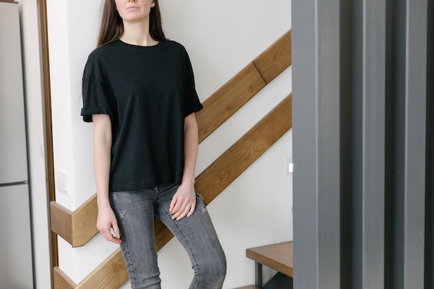 Mujer con camiseta negra en blanco con espacio para su logotipo, maqueta o diseño en interiores